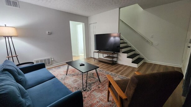 A living room with a sofa, a coffee table, a TV on a stand, a lamp, and a staircase. - King Bed| Pet Friendly |2BR Townhome with Parking (Louisville)