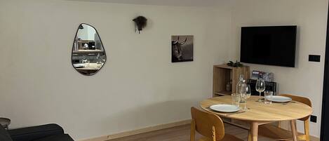 A modern living room with a dark grey sofa, a wooden dining table with chairs, a mounted TV, and a mirror on the wall.