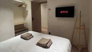Une chambre moderne avec un lit, un téléviseur fixé au mur et une échelle en bois.