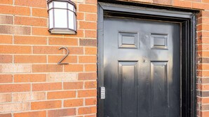 A black door with a number '2' above it, a metal doorbell, and a wall-mounted light fixture.
