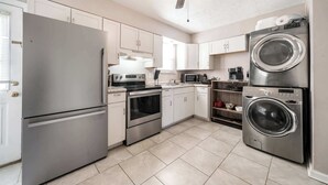 A modern kitchen with stainless steel appliances, white cabinets, and a ceiling fan.