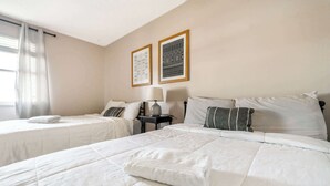 A hotel room with two beds, a nightstand with a lamp, and two framed pictures on the wall.