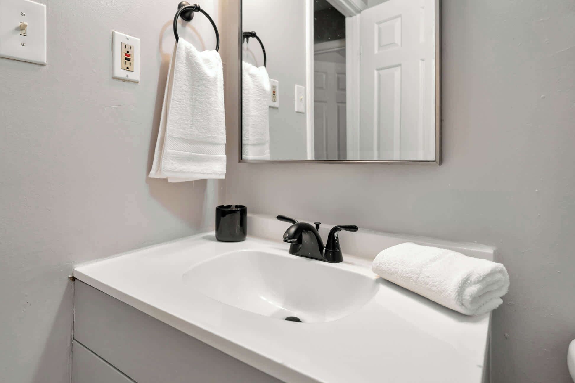 A bathroom with a white sink, a mirror, and two towels hanging on hooks.