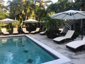 Ein Poolbereich mit Liegestühlen und Sonnenschirmen, umgeben von Palmen.