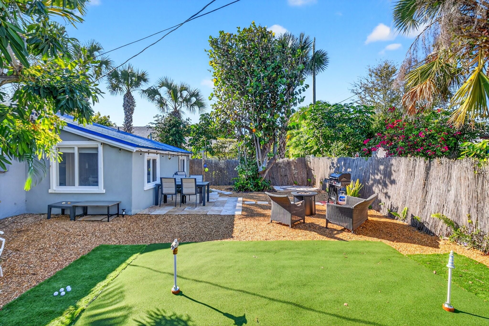 Un patio trasero con césped, una casa pequeña, mobiliario de exterior y una valla de madera.