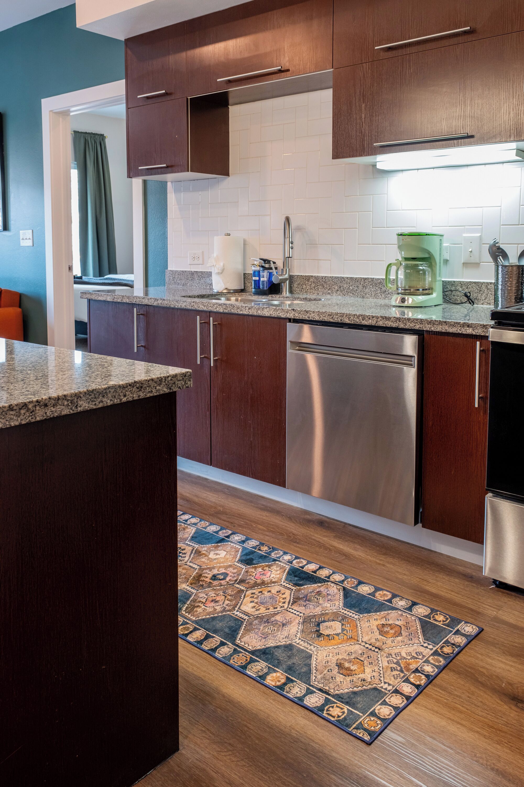 A modern kitchen with wooden cabinets, stainless steel appliances, and a patterned rug.