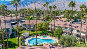 A resort with a swimming pool surrounded by palm trees and houses with red-tiled roofs.