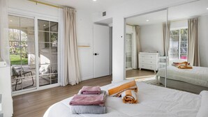 A modern bedroom with a large bed, a sliding glass door to a balcony, and a mirrored closet.