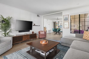 Ein modernes Wohnzimmer mit Flachbildfernseher, grauen Sofas, einem Couchtisch und einem Essbereich mit Stühlen und Tisch.