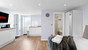 Un appartamento moderno con cucina, zona soggiorno dotata di divano e televisore, e bagno parzialmente visibile attraverso una porta aperta.