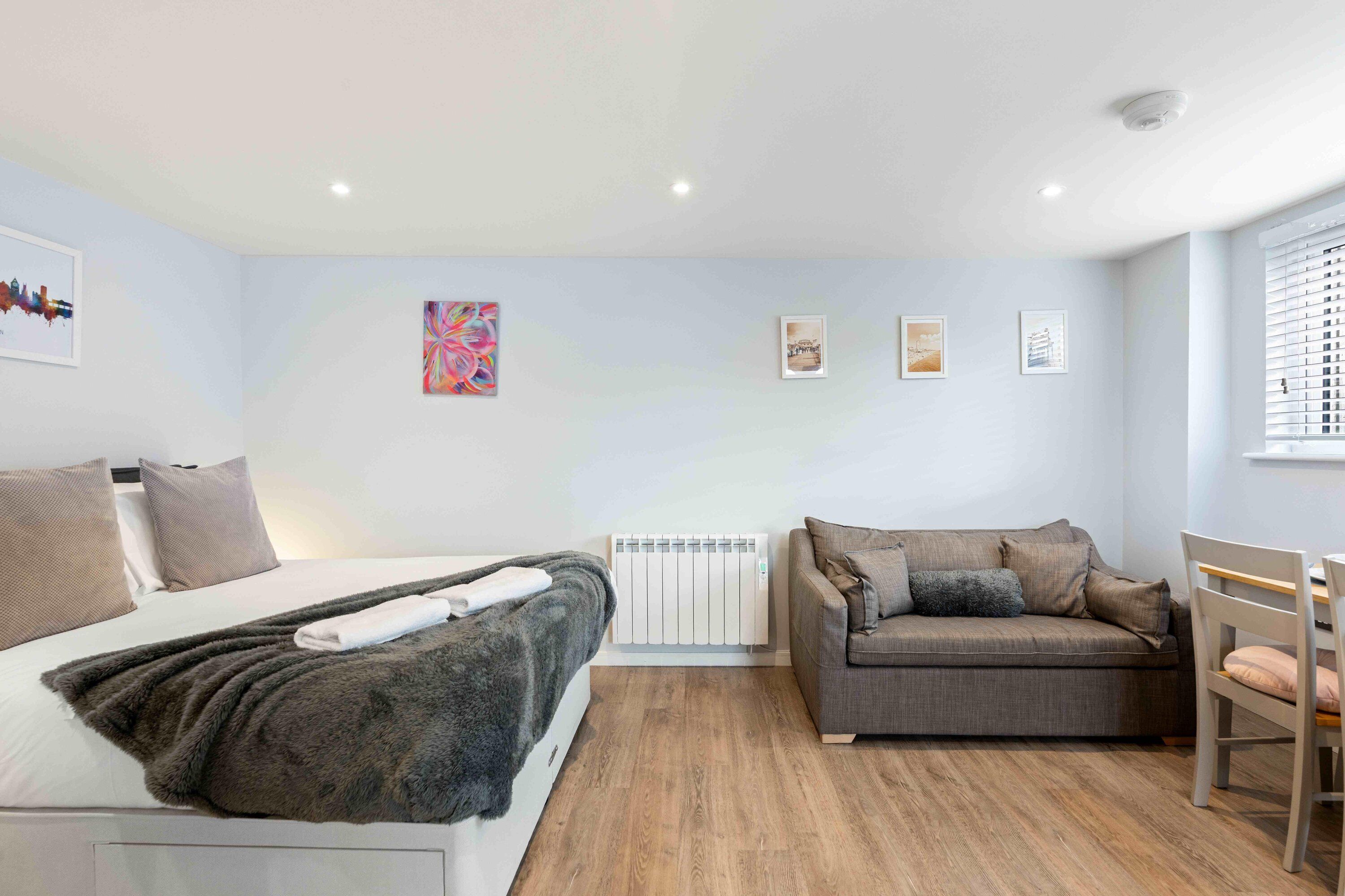 A modern bedroom with a bed, a grey sofa, a wooden floor, and a radiator.