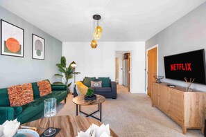 A modern living room with a green sofa, a coffee table, a TV displaying 'NETFLIX', and a wicker cabinet. - Queens Cove With Seaviews By My Getaways (Worthing)