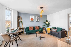 A modern living room with a green sofa, a coffee table, and a dining area with chairs and a table. - Queens Cove With Seaviews By My Getaways (Worthing)