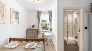 A bedroom with a bed, a desk, a dresser, and a shower area. - Queens Cove With Seaviews By My Getaways (Worthing)