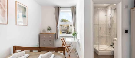 A bedroom with a bed, a desk, a dresser, and a shower area.