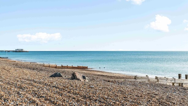 A pebbled beach with a wooden walkway and a pier in the background. - Queens Cove With Seaviews By My Getaways (Worthing)