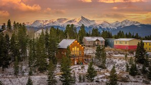 Un albergue de montaña con varias edificaciones, rodeado de árboles nevados y montañas al fondo.