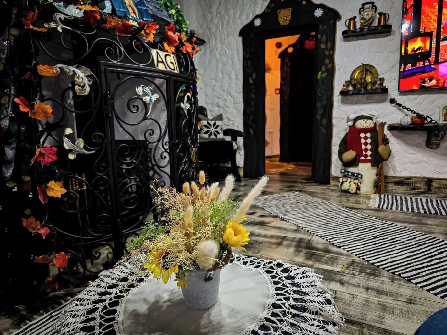 A cozy room with a decorative black gate labeled "AGI," a small table with a crocheted doily, and a television displaying a colorful scene.