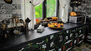 A kitchen with a black countertop, white curtains, a fruit bowl, and a microwave.