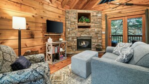 A cozy cabin interior with a stone fireplace, wooden walls, a flat-screen TV, and a comfortable seating area. - Great For Couples.. Great Location! Cozy log cabin w/ NEW Hot Tub! 8 Min to Dtwn (Gatlinburg)