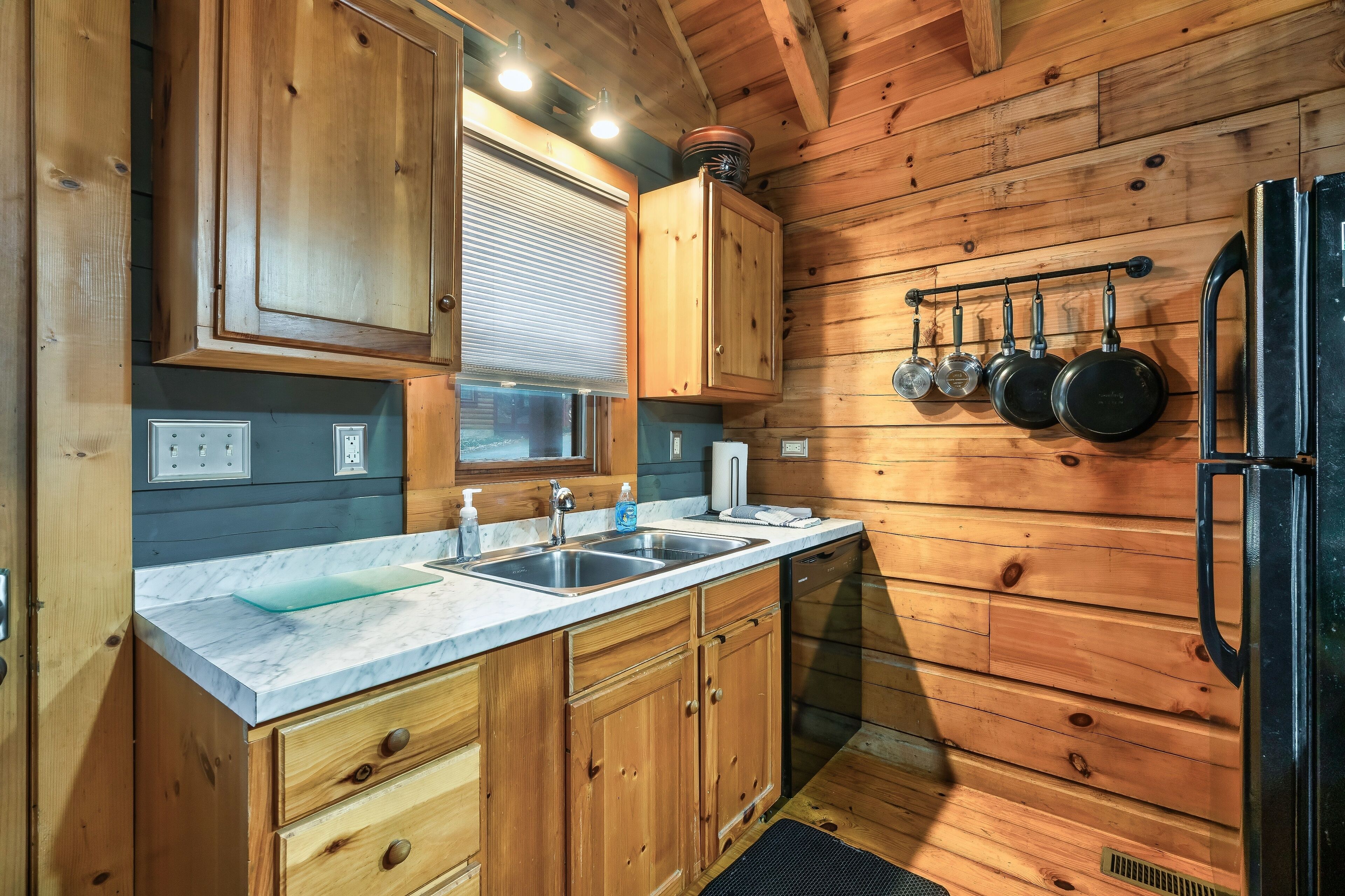 A kitchen with wooden cabinets, a marble countertop, a sink, and a refrigerator.