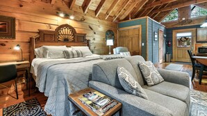 A cozy cabin-style room with a large bed, a sofa, and a desk. - Great For Couples.. Great Location! Cozy log cabin w/ NEW Hot Tub! 8 Min to Dtwn (Gatlinburg)