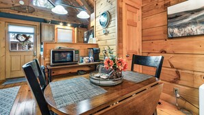 A wooden interior with a dining table, chairs, a clock, and a painting on the wall. - Great For Couples.. Great Location! Cozy log cabin w/ NEW Hot Tub! 8 Min to Dtwn (Gatlinburg)