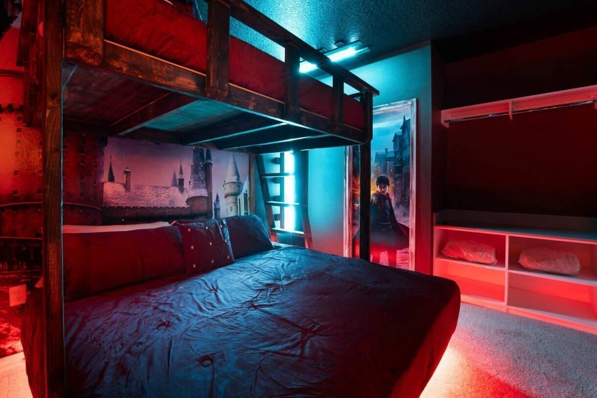 A bunk bed room with a red and blue color scheme, a wooden ceiling, and a window with a view of a castle.