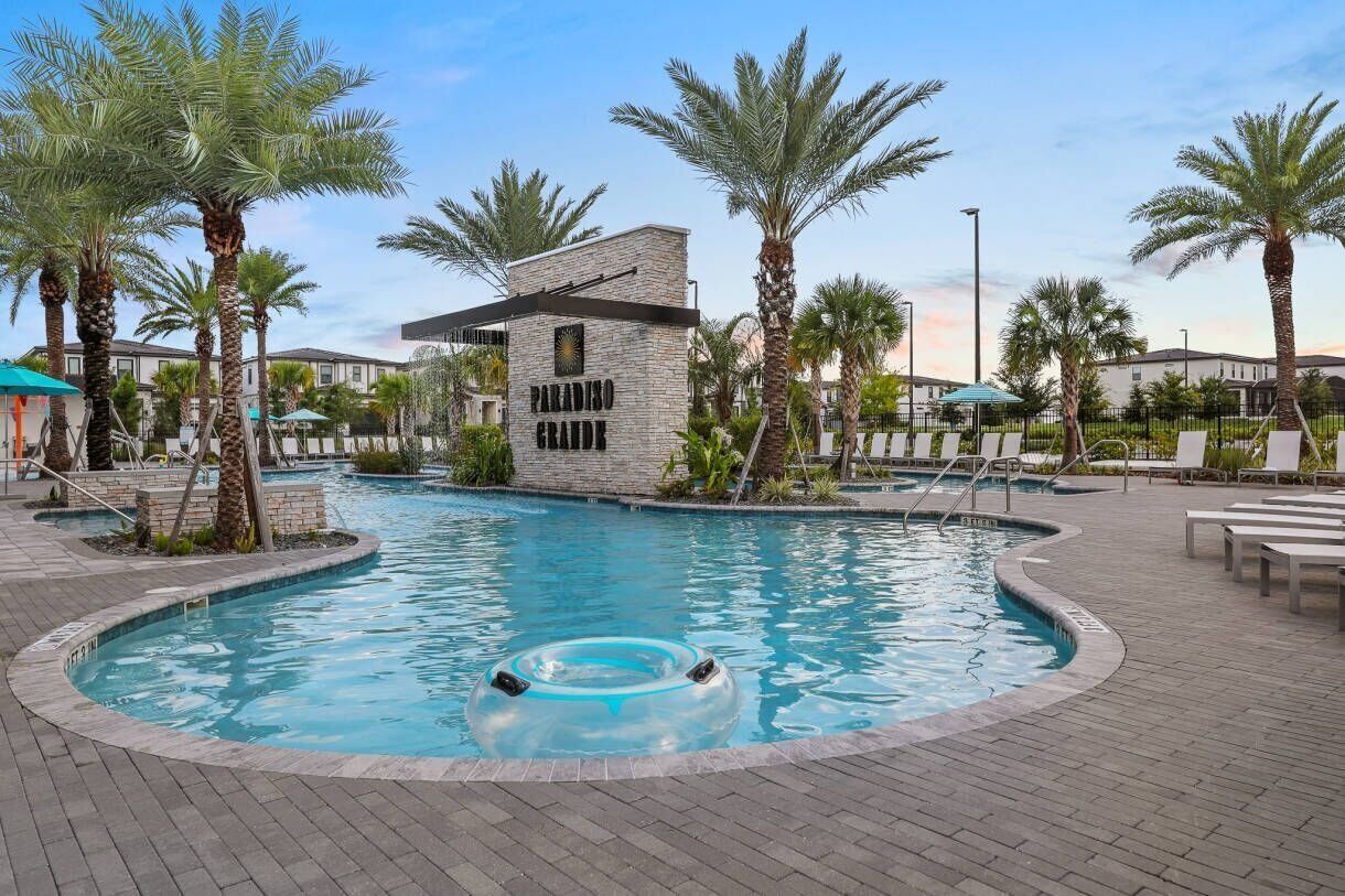 A swimming pool with a stone building labeled "PARADISO GRANDE" in the center, surrounded by palm trees and lounge chairs.