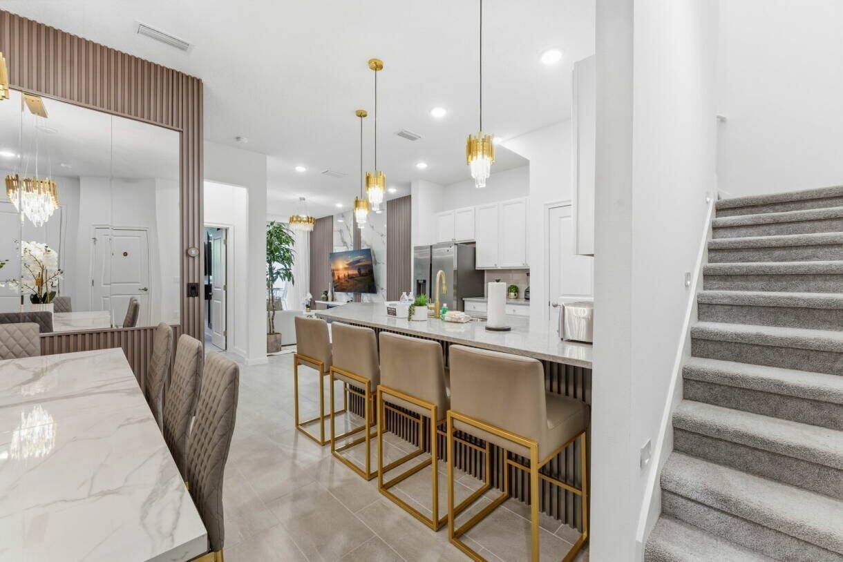 A modern kitchen with a central island, pendant lights, and a staircase.