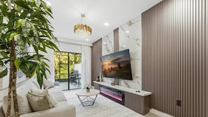 A modern living room with a large TV, a sofa, a coffee table, and a plant. - Paradiso Grande 5BR Home w Pool, Mario Game Room (Orlando)