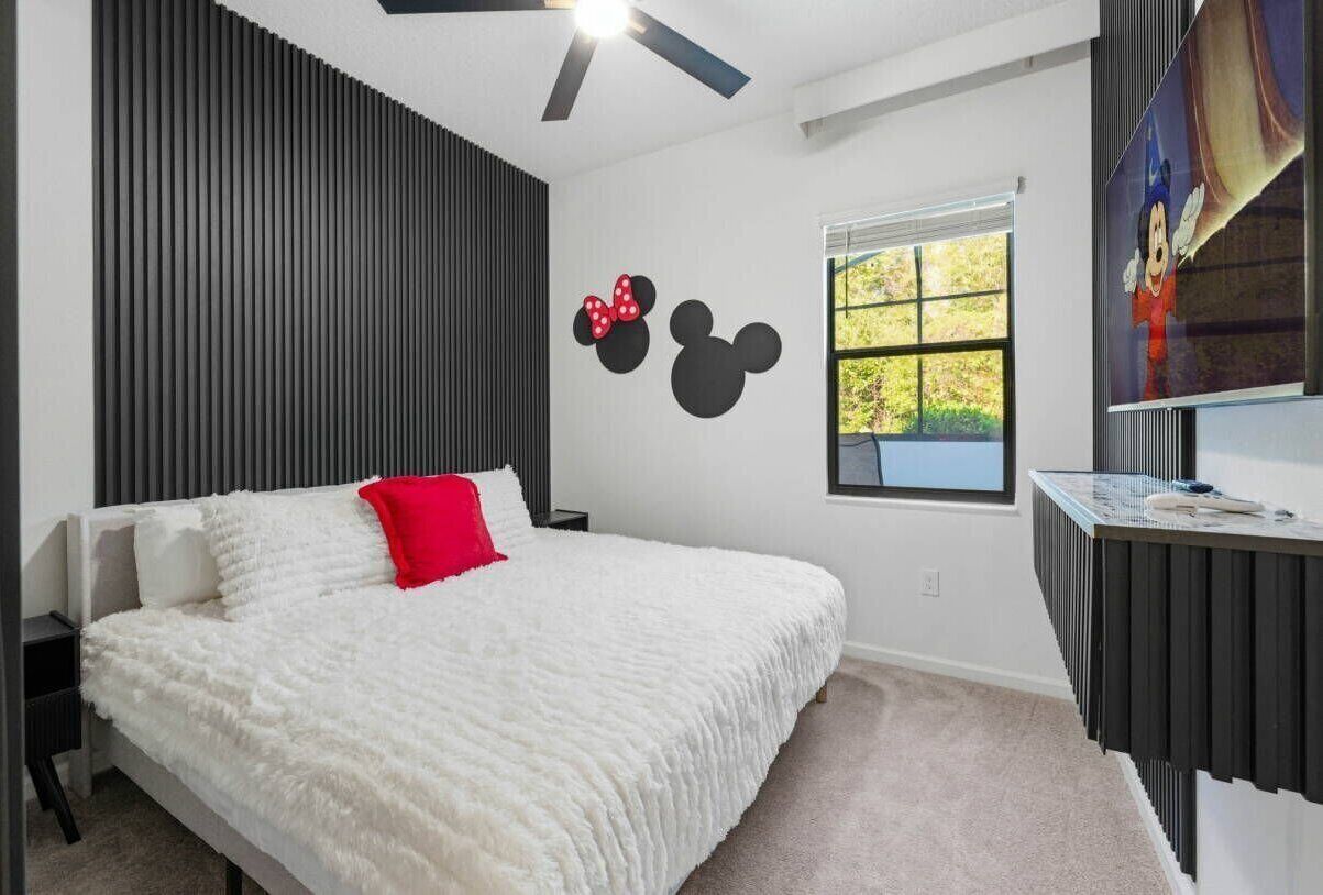 Ein Schlafzimmer mit einem Bett, einer Wanddekoration mit Mickey Mouse, einem Fenster mit Ausblick und einem Deckenventilator.