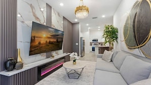 A modern living room with a large flat-screen TV, a sofa, a coffee table, and a chandelier. - Paradiso Grande 5BR Home w Pool, Mario Game Room (Orlando)