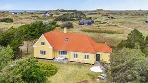 Una casa amarilla con techo rojo, rodeada de vegetación y otras casas en un entorno rural.