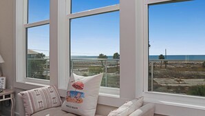 A room with large windows, a view of the beach, and a cushion with a beach design. - Abalonian House (Port St. Joe)