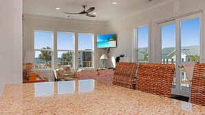 A spacious living room with a large window, a ceiling fan, and a television on the wall. - Abalonian House (Port St. Joe)