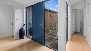 En modern inredning med en skjutdörr i glas som leder ut till ett utomhusområde, en stor, mörk vas på golvet och ett trästaket som syns genom dörren.