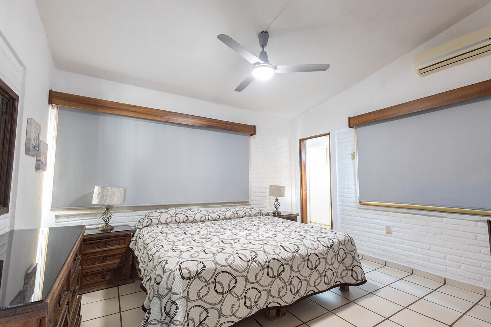 Une chambre à coucher avec un lit, deux tables de chevet, un ventilateur de plafond et une fenêtre.