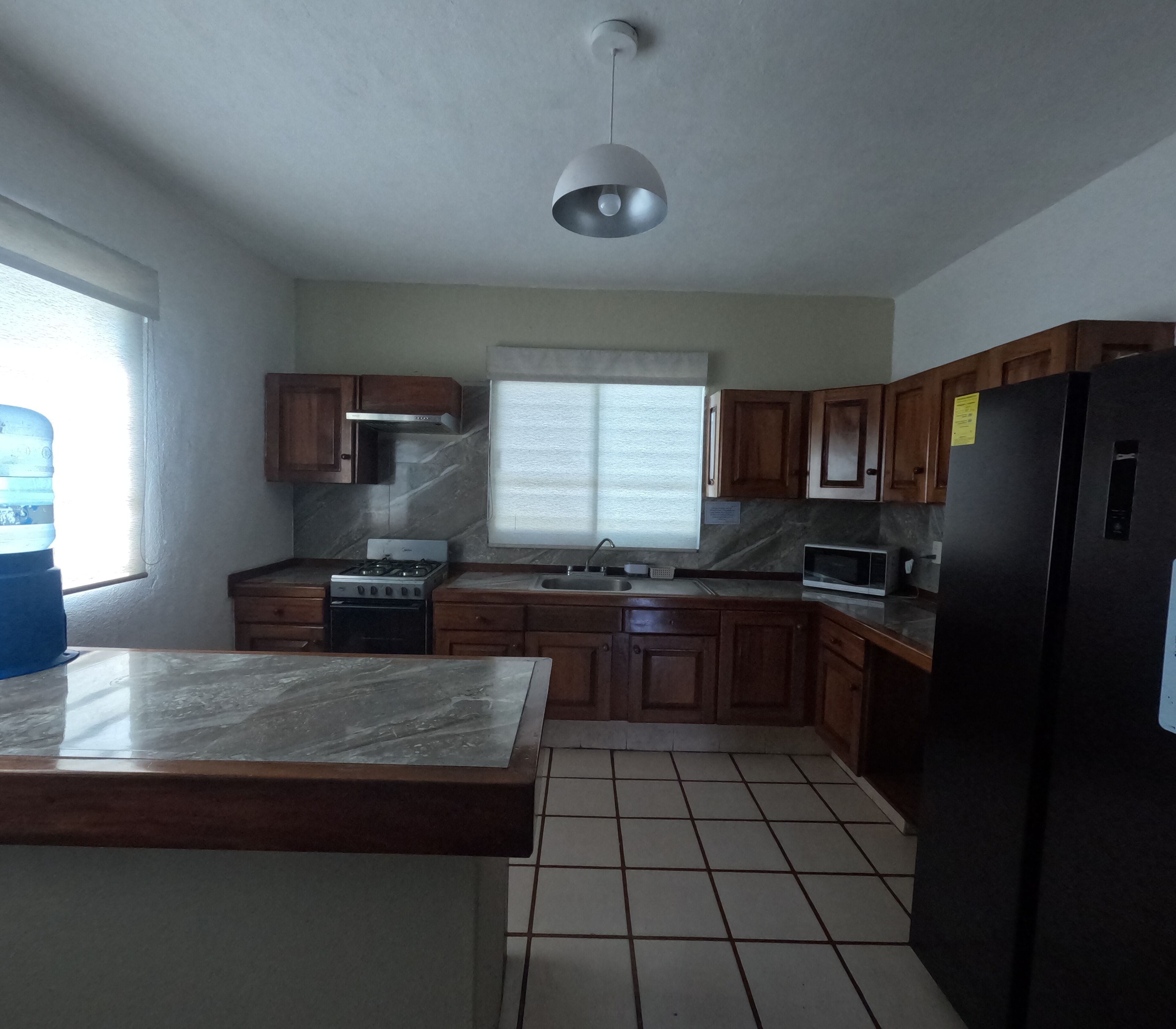 A kitchen with wooden cabinets, a black refrigerator, a stove, and a window with blinds.