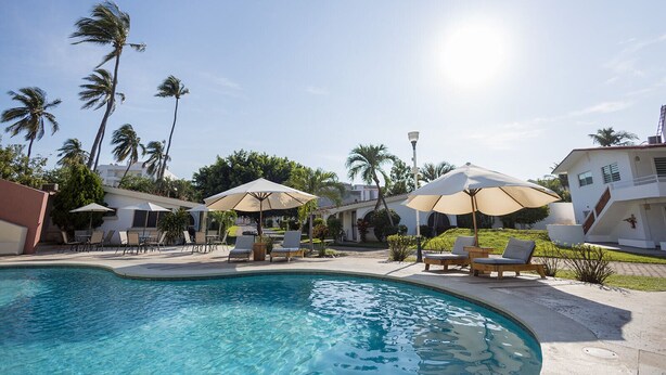 Zwembad met ligbedden en parasols, omgeven door palmbomen en een heldere lucht.