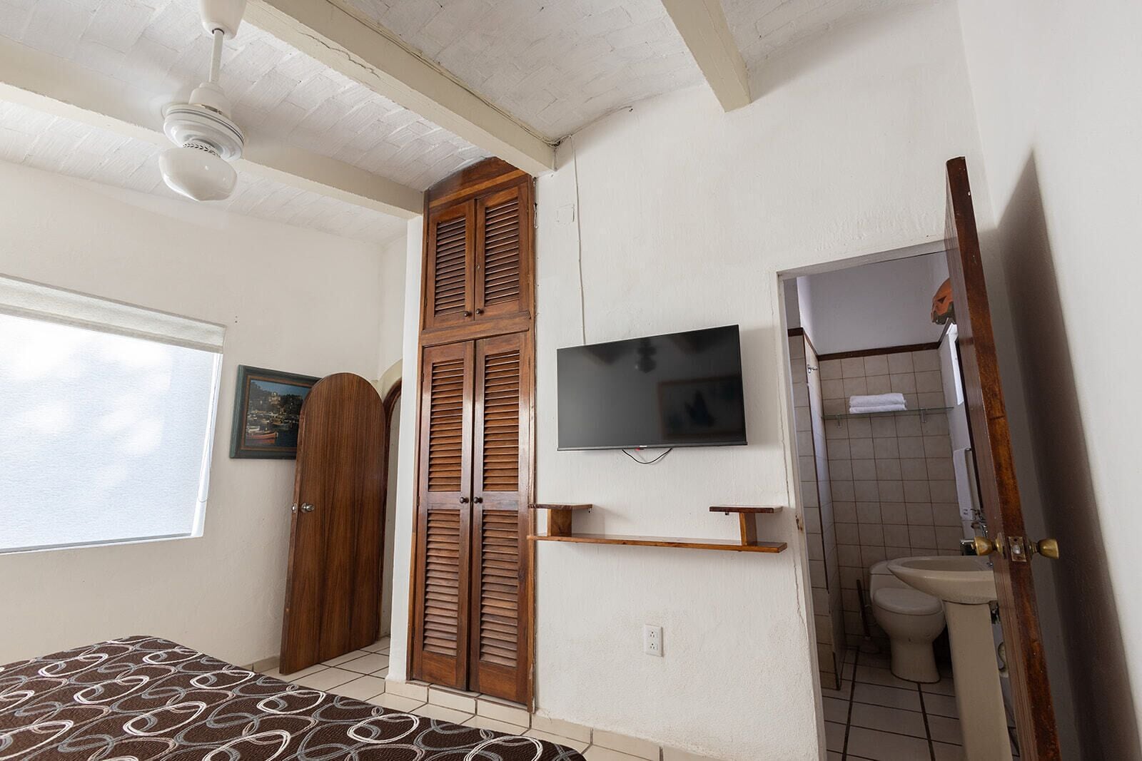 Un dormitorio con cama, armario, televisor y baño con inodoro y lavamanos.