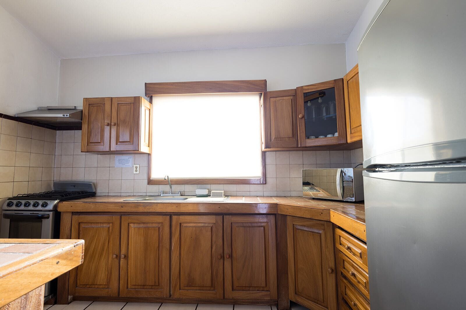 A kitchen with wooden cabinets, a stainless steel refrigerator, a built-in oven, and a window above the sink.