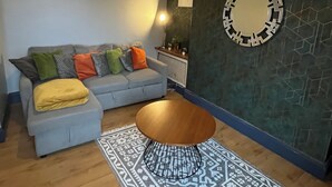 A living room with a grey sofa, a wooden coffee table, a patterned rug, a wall-mounted mirror, and a pendant light. - garden flat in vibrant area of Clifton  by Bristol university (Bristol)