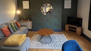 A modern living room with a grey sofa, a blue armchair, a coffee table, a TV stand, and a decorative mirror. - garden flat in vibrant area of Clifton  by Bristol university (Bristol)
