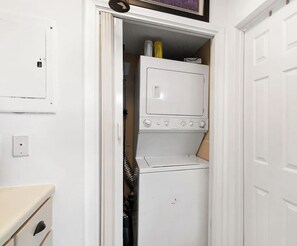 A compact laundry room with a washer and dryer, a small cabinet, and a door with a handle. - 1-Bedroom Salty Escape Condo with pool and Lagoon view with boat launch and dock (Gulf Shores)