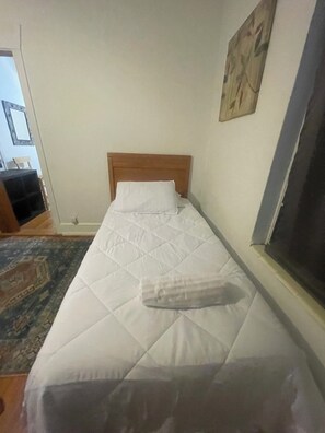 A single bed with a wooden headboard in a room with a plain white wall and a patterned rug. - Enjoyable House just minutes from Downtown, FSU & FAMU 2 of 2  (Tallahasse)