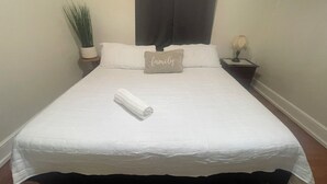 Ein ordentlich bezogenes Bett mit einem zusammengerollten Handtuch, einem Kissen mit dem Schriftzug "family" und einer kleinen Pflanze auf einem Nachttisch.