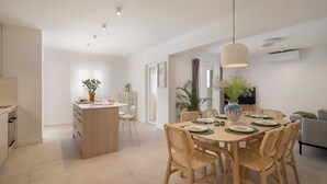 Een moderne keuken met een centraal eiland, een eethoek met rieten stoelen en een televisie in de woonkamer.