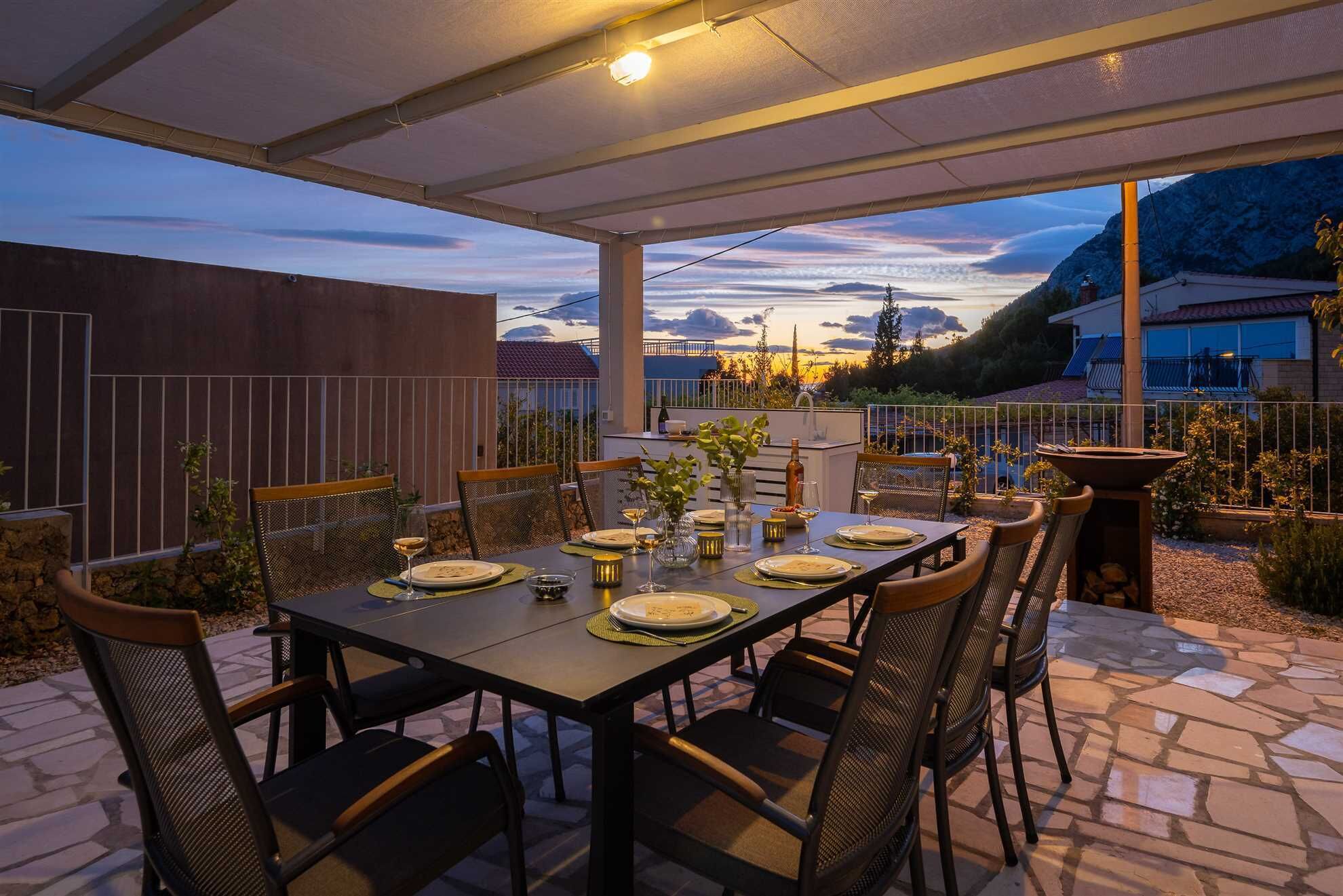 An outdoor dining area with a table set for four, surrounded by chairs, under a covered patio.