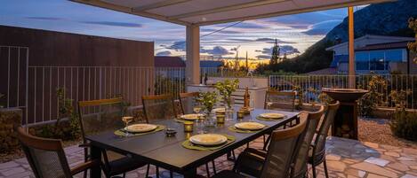 An outdoor dining area with a table set for four, surrounded by chairs, under a covered patio.